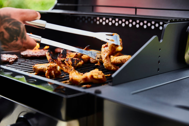 Close-up of chicken wings on the Swan BBQ being flipped with the Swan BBQ Tongs