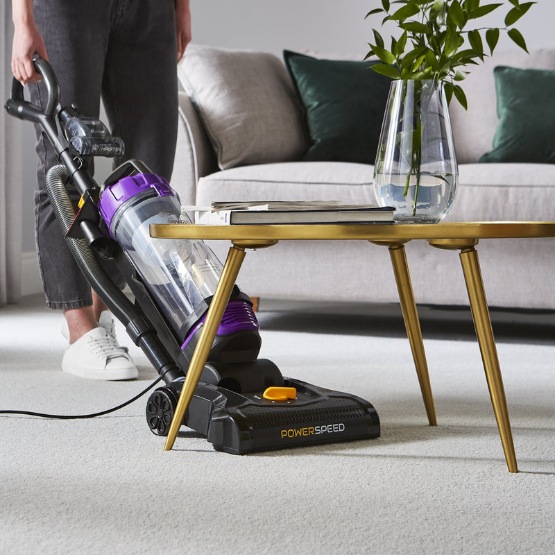 Woman using the Swan Powerspeed Upright Pet Extend Vacuum to vacuum underneath her living room table