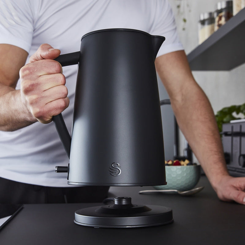 Photograph of man holding up Swan 1.7 Litre Stealth Kettle above black kettle stand in a modern kitchen