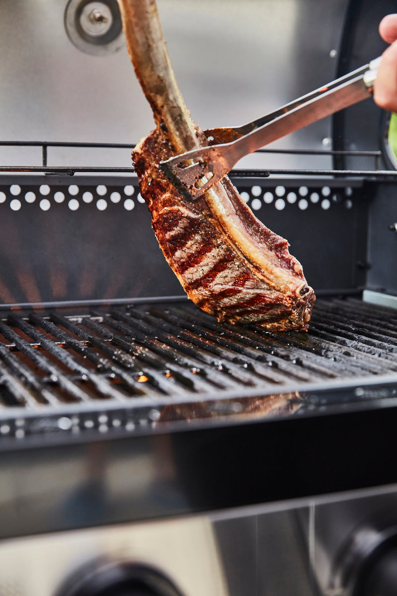 Close-up of a pork rib being flipped on the Swan Kansas BBQ by a pair of tongs from the Swan BBQ Tool Set