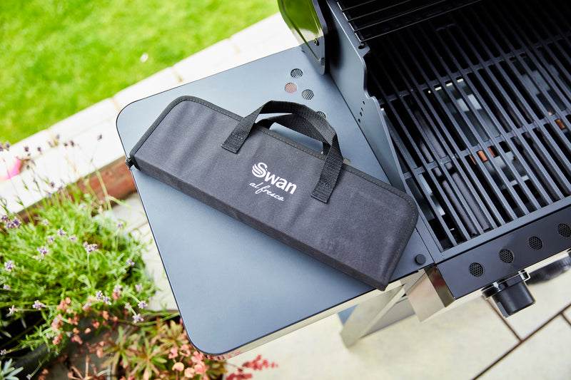 Swan BBQ Tool Set in Swan black bag on top of Swan Kansas 3 Burner Gas BBQ with Side Burner in green garden