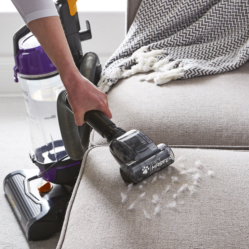 Woman using the Swan Powerspeed Upright Pet Extend Vacuum to vacuum pet fur off of a cream sofa
