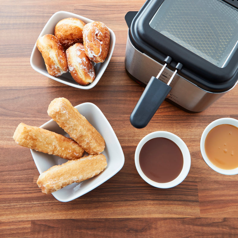 Birdseye view of the Swan 1.5 Litre Stainless Steel Fryer next to fried churros, doughnuts and dessert sauces on a wooden countertop