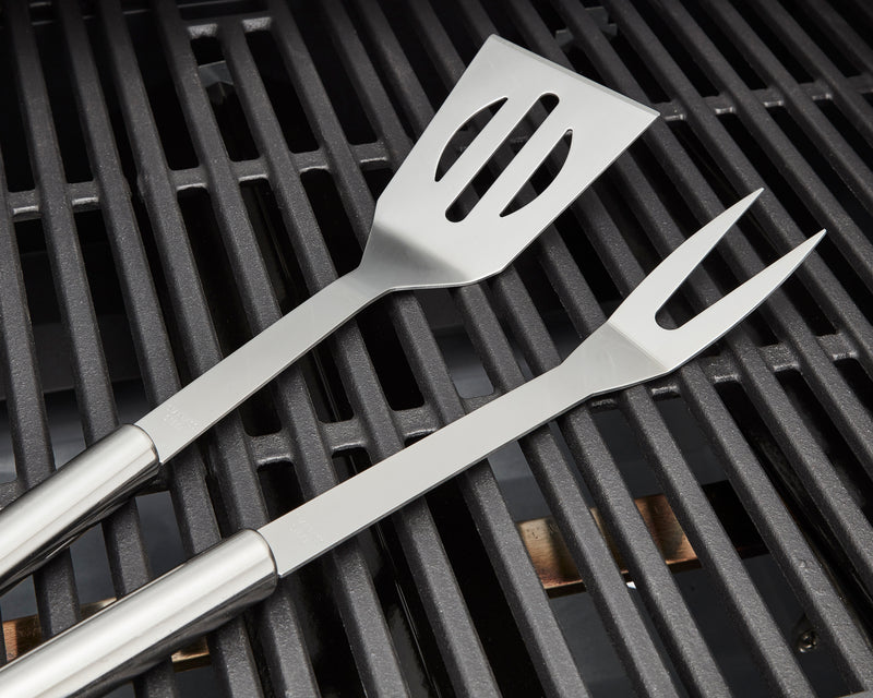 Close up of silver spatula and silver pronged fork from the Swan BBQ Tool Set on grill